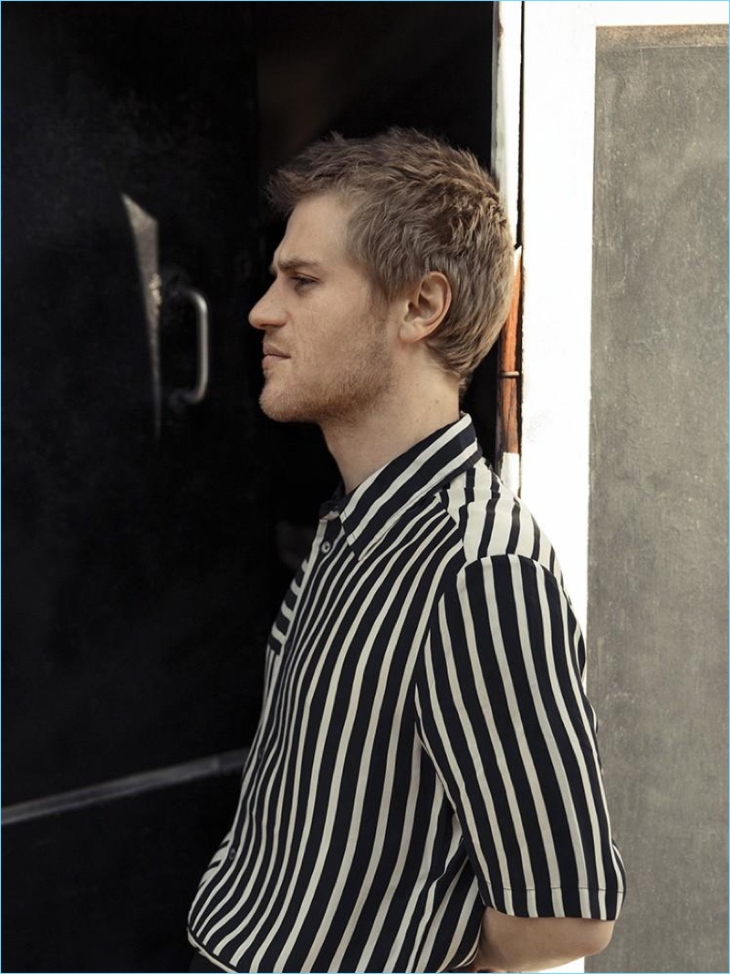 Delivering a side profile, Johnny Flynn wears a striped shirt from McQ by Alexander McQueen.