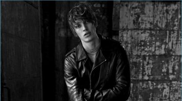 Near Night: Lucas Satherley Models Dark Fashions for Essential Homme Sitting for a black and white photo, Lucas Satherley wears a Rick Owens leather biker jacket with an Officine Generale t-shirt. He also sports Dolce & Gabbana trousers with Dior Homme shoes.