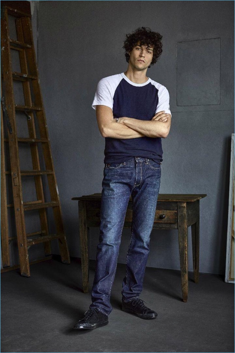 Crossing his arms, Miles McMillan sports a Todd Snyder + Champion color blocked raglan tee $65 and Todd Snyder indigo wash selvedge denim jeans $248.