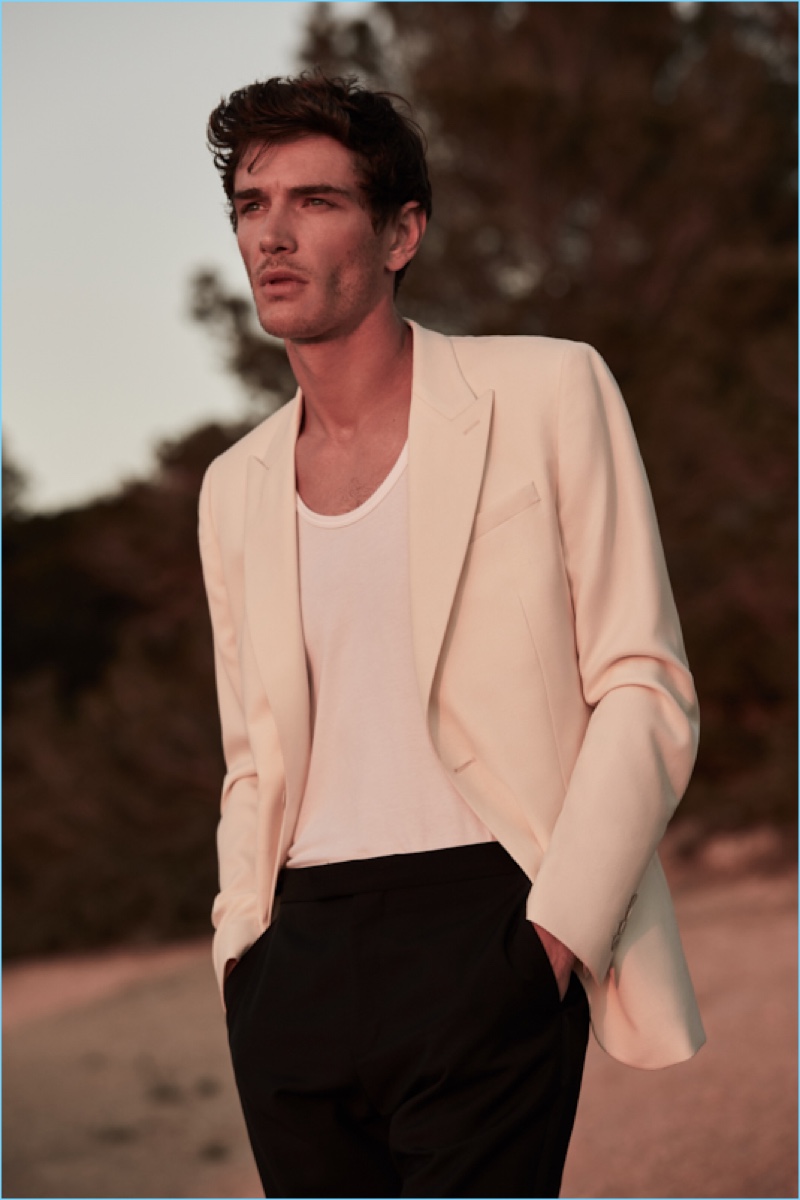 A sleek summer vision, Julien Sabaud dons a Reiss off-white slim peak lapel blazer $555 with a short-sleeve sweater $145. The French model also wears Reiss tuxedo trousers.