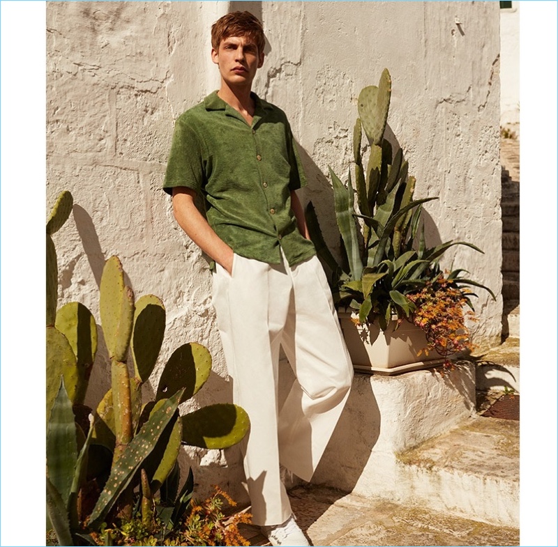 A chic vision, Baptiste Radufe wears a green short-sleeved French terry cloth shirt $215 by Hecho with wide-leg Tomorrowland trousers $207, and suede AMI sneakers $296.
