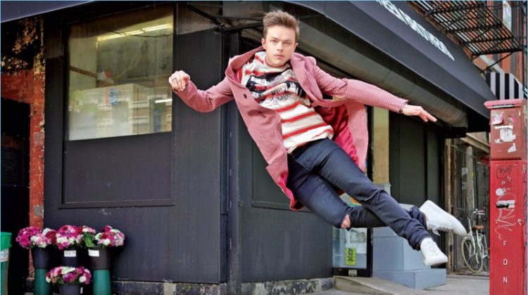 Leaping, Dane DeHaan wears a Stella McCartney t-shirt with a Prada overcoat. He also sports Saint Laurent jeans and Common Projects sneakers.