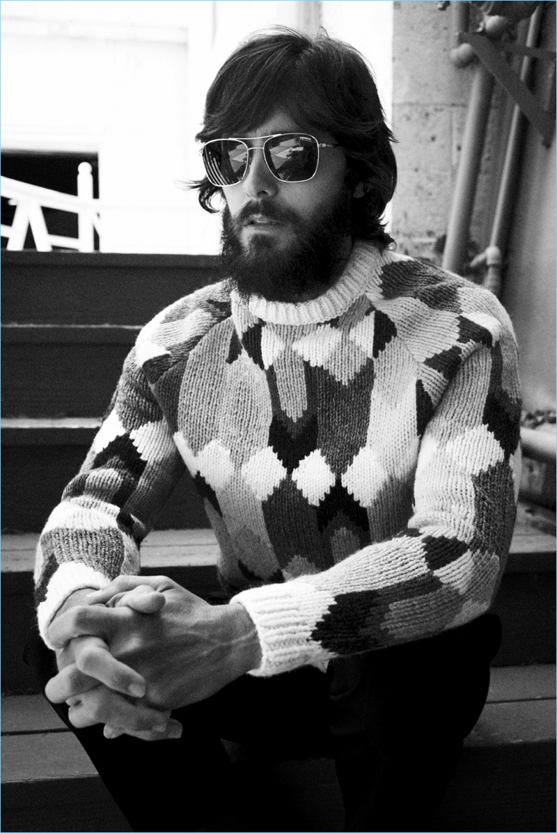 Appearing in a black and white image, Jared Leto wears a Prada sweater and trousers with Carrera sunglasses.