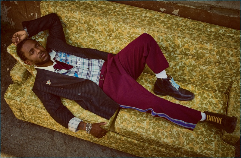 Relaxing, Kendrick Lamar wears a pinstripe jacket, side stripe trousers, and boots by Gucci. He also rocks a Lanvin shirt and Adidas Originals by Alexander Wang polo.