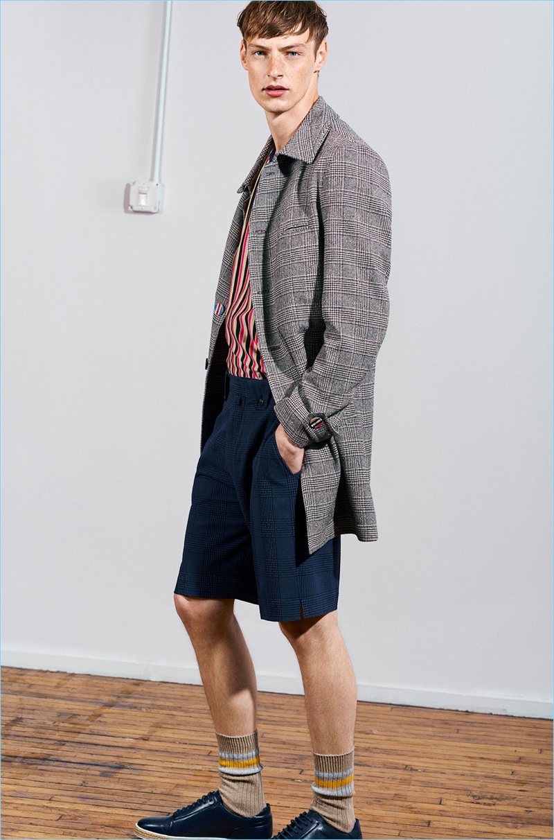 Roberto Sipos models an overcoat, t-shirt, checked Bermuda shorts, striped socks, and leather shoes from Zara Man's Studio collection.