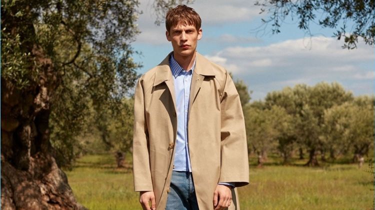 French model Baptiste Radufe dons a Mackintosh trench coat with a striped Commes des Garçons Shirt striped shirt. His look is complete with Balenciaga jeans and AMI shoes.
