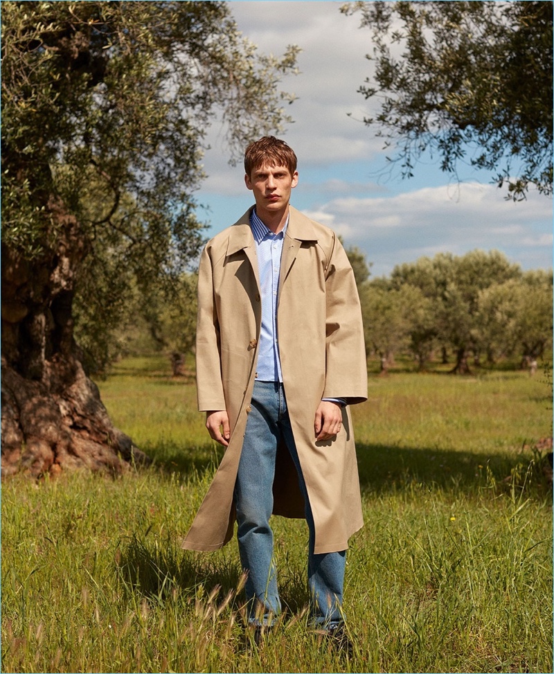 French model Baptiste Radufe dons a Mackintosh trench coat with a striped Commes des Garçons Shirt striped shirt. His look is complete with Balenciaga jeans and AMI shoes.