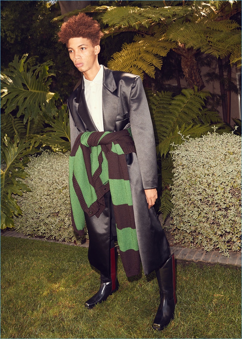 Formal and casual style collide. Tay Godsey models a Raf Simons satin coat and pants. He also wears a Raf Simons shirt and cardigan sweater. Calvin Klein 205W39NYC western boots complete his look.