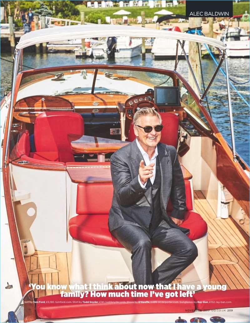 Riding on a boat, Alec Baldwin dons a Tom Ford suit with a Todd Snyder shirt. All smiles, he wears Ray-Ban sunglasses.