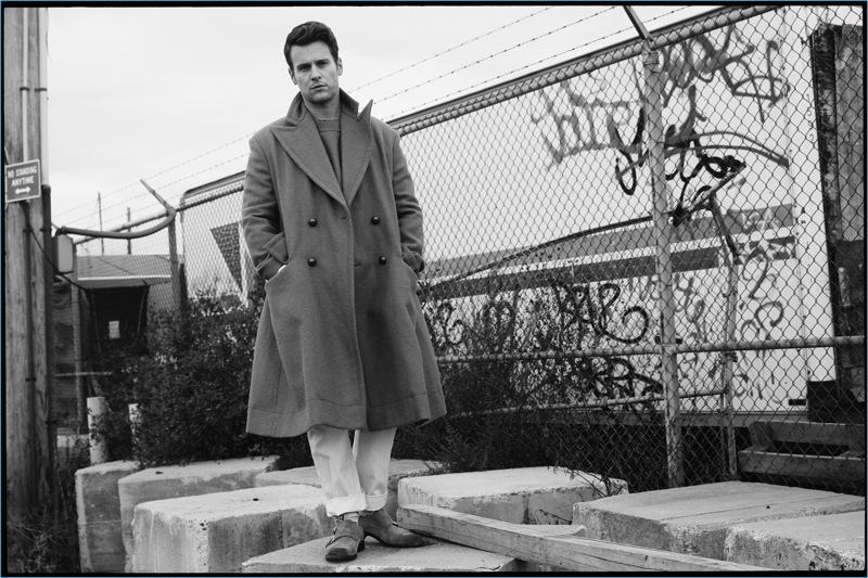 Donning an oversized Vivienne Westwood coat, Jonathan Groff also wears a sweater and pants by the brand. Groff sports a Cotton Citizen shirt, Gucci socks, and O'Keeffe shoes as well.