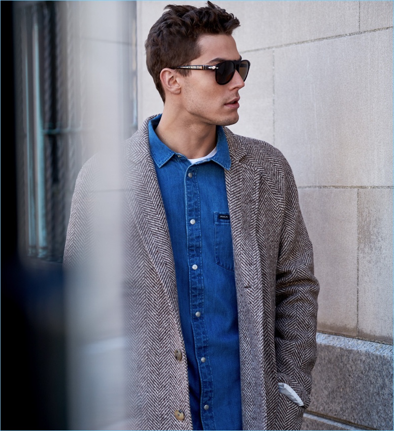 Jacob Hankin wears a Calvin Klein t-shirt, RVCA denim shirt, and De Bonne Facture coat. He also sports J Brand jeans with Persol sunglasses.