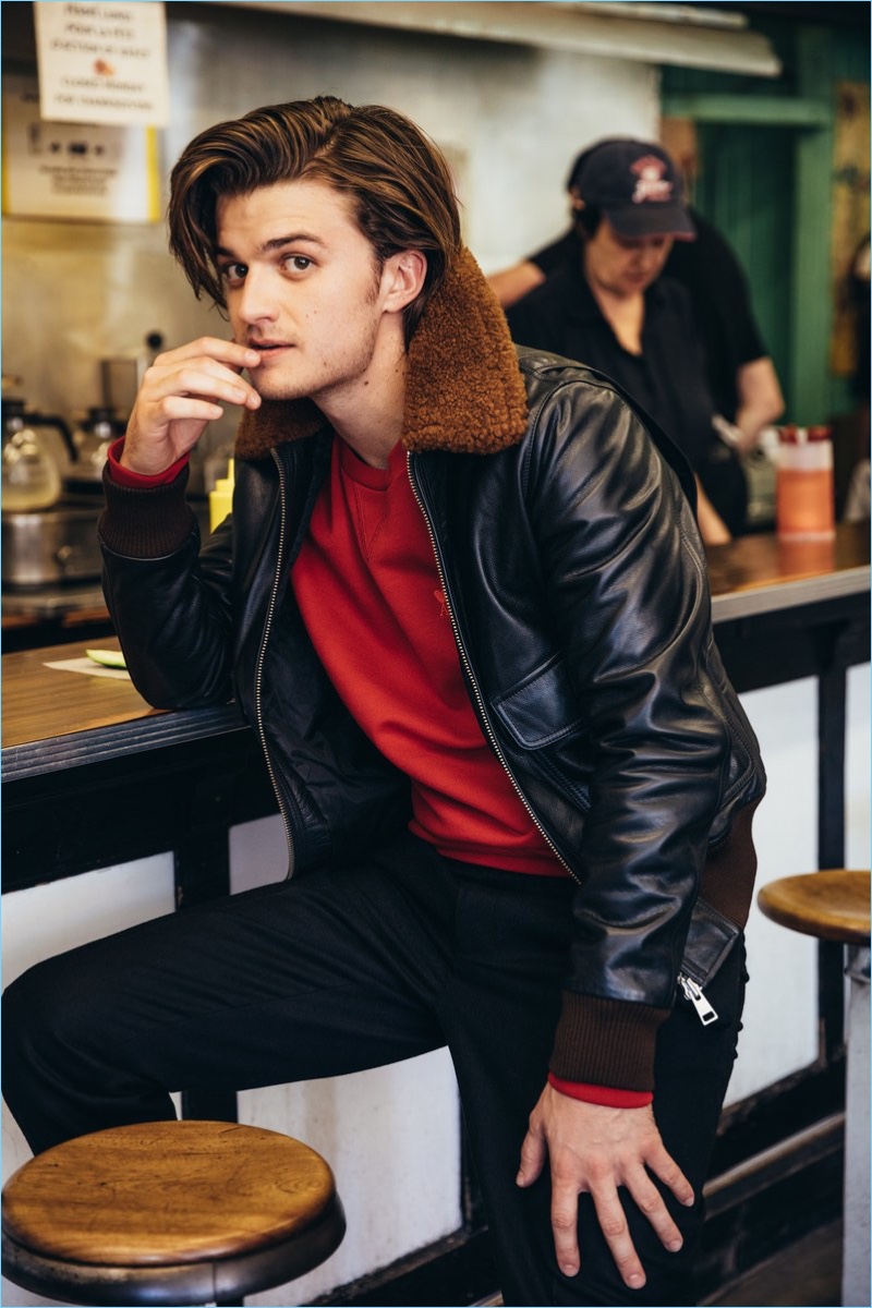 A cool vision, Joe Keery wears a red sweatshirt and shearling leather bomber jacket by AMI. He also sports Moncler trousers and Common Projects sneakers.
