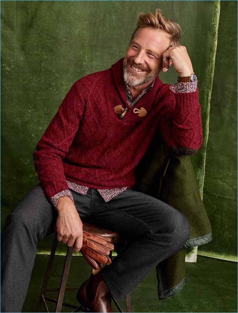 All smiles, Rainer Andreesen wears a shawl neck sweater with a printed shirt and trousers.