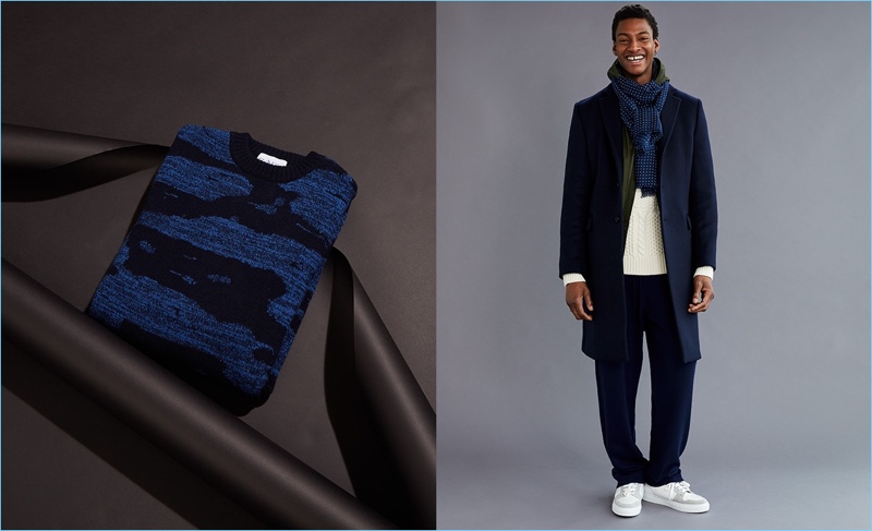 All smiles, Ty Ogunkoya wears an Acne Studios coat, Prada jacket, Burberry sweater, and Allude track pants. A Dunhill scarf and AMI sneakers complete his look. An oversized sweater by Raey appears left.
