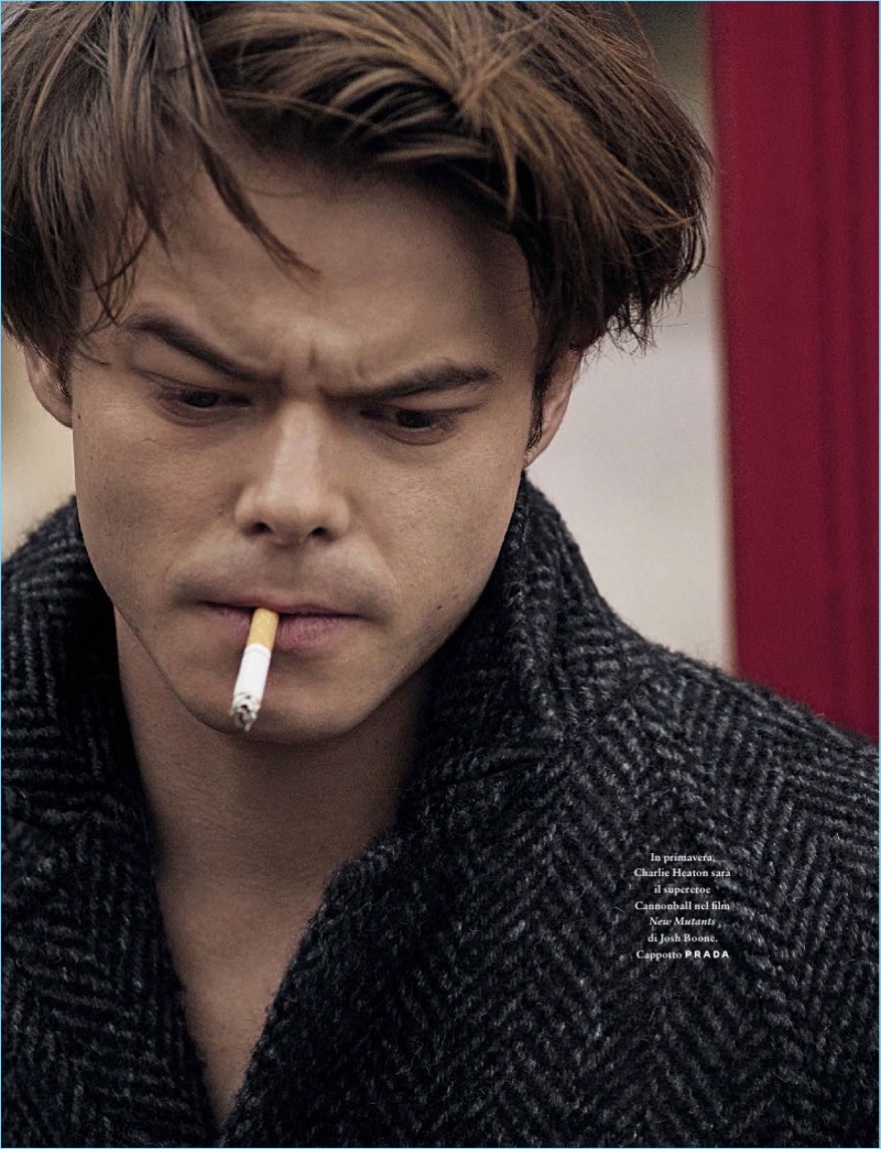 Smoking a cigarette, Charlie Heaton wears a Prada coat.