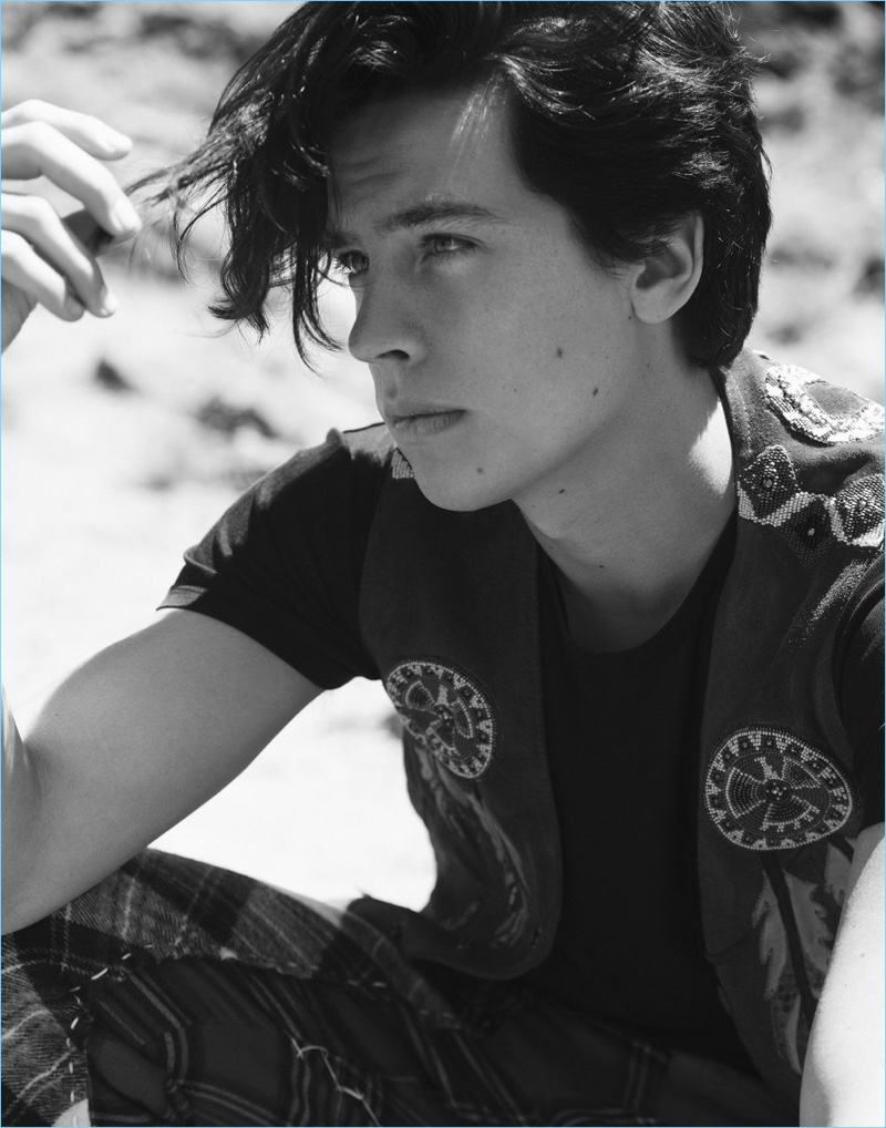 Appearing in a black and white picture, Cole Sprouse wears a Roberto Cavalli vest. The young actor also rocks a Saint Laurent t-shirt and Loewe pants.