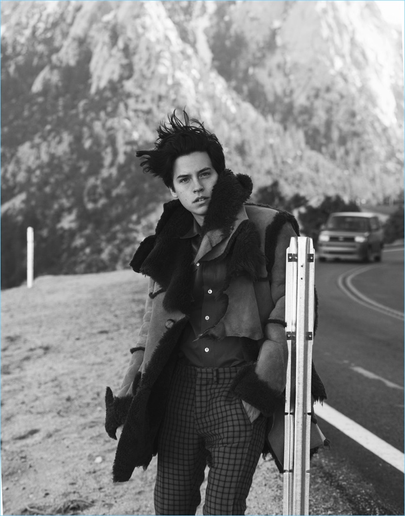 Taking to the side of the road, Cole Sprouse dons a Coach coat and pants with a Roberto Cavalli shirt.