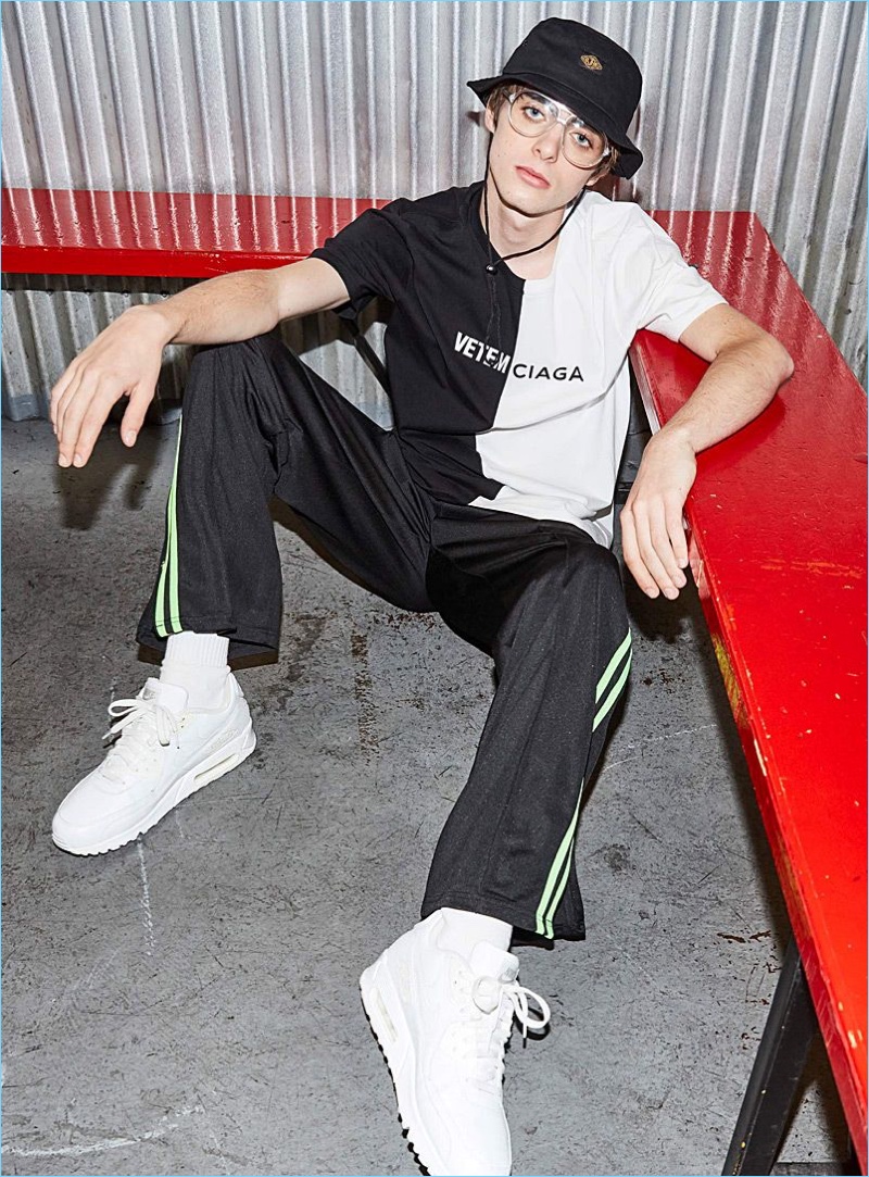 Connecting with Simons, Lennon Gallagher wears a DJAB spliced t-shirt and logo bucket hat. The model also sports IC.Story track pants and white Nike Air Huarache Run Ultra sneakers.