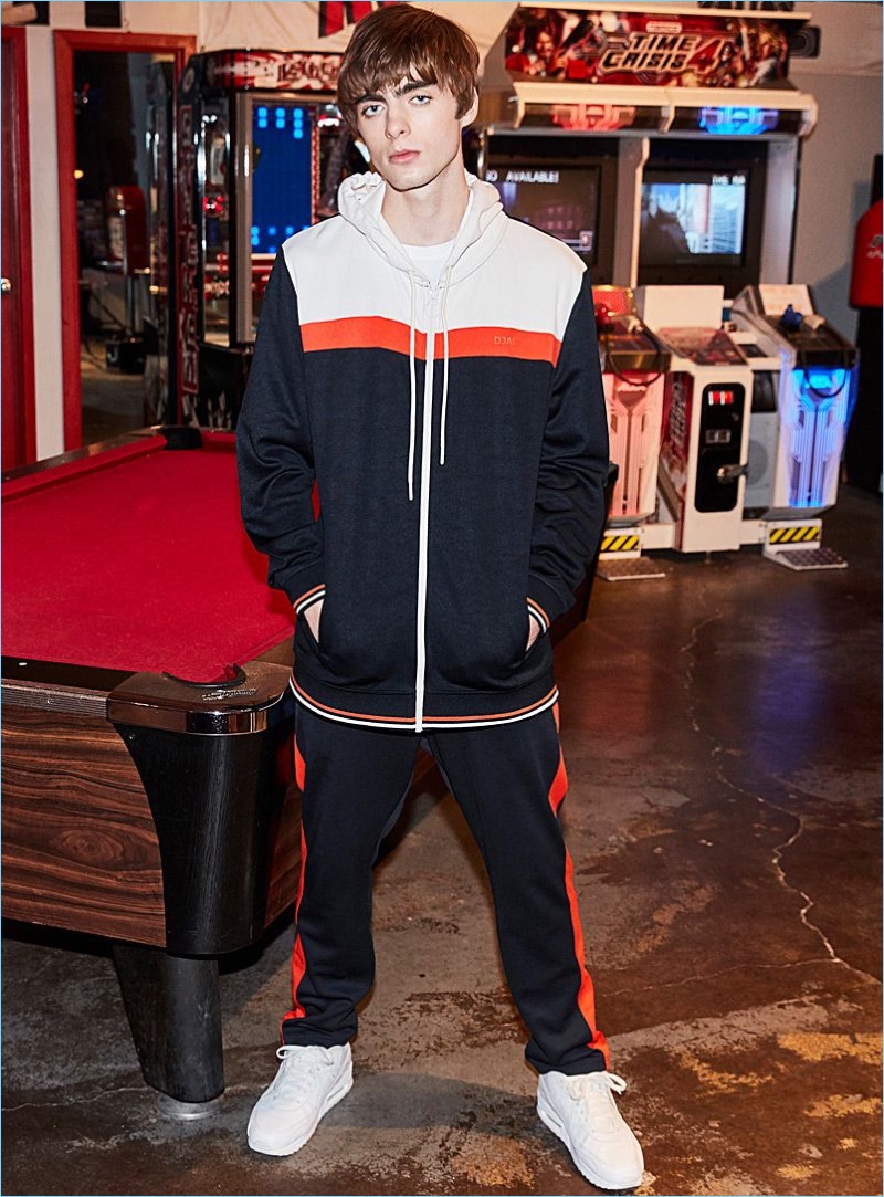 Lennon Gallagher rocks a DJAB athletic jacket and striped track pants with Reebok Classic sneakers in white.