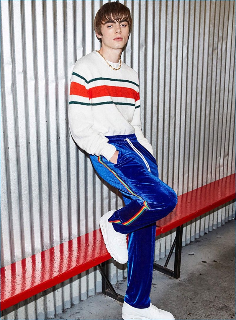 Embracing retro style, Lennon Gallagher wears a DJAB stripe sweater with IC.Story rainbow-stripe velvet track pants, and Nike Air Huarache Run Ultra sneakers.