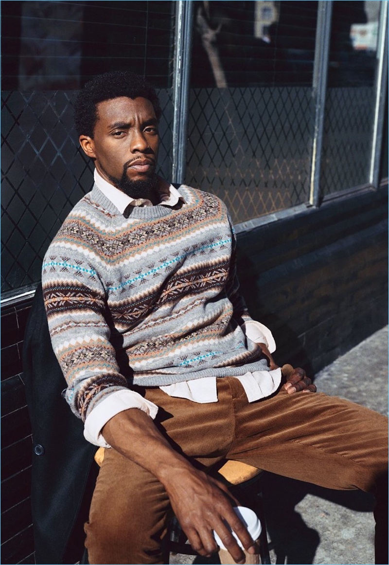 Sitting for a picture, Chadwick Boseman wears a J.Crew fair isle sweater, Our Legacy shirt, and Oliver Spencer corduroy trousers.