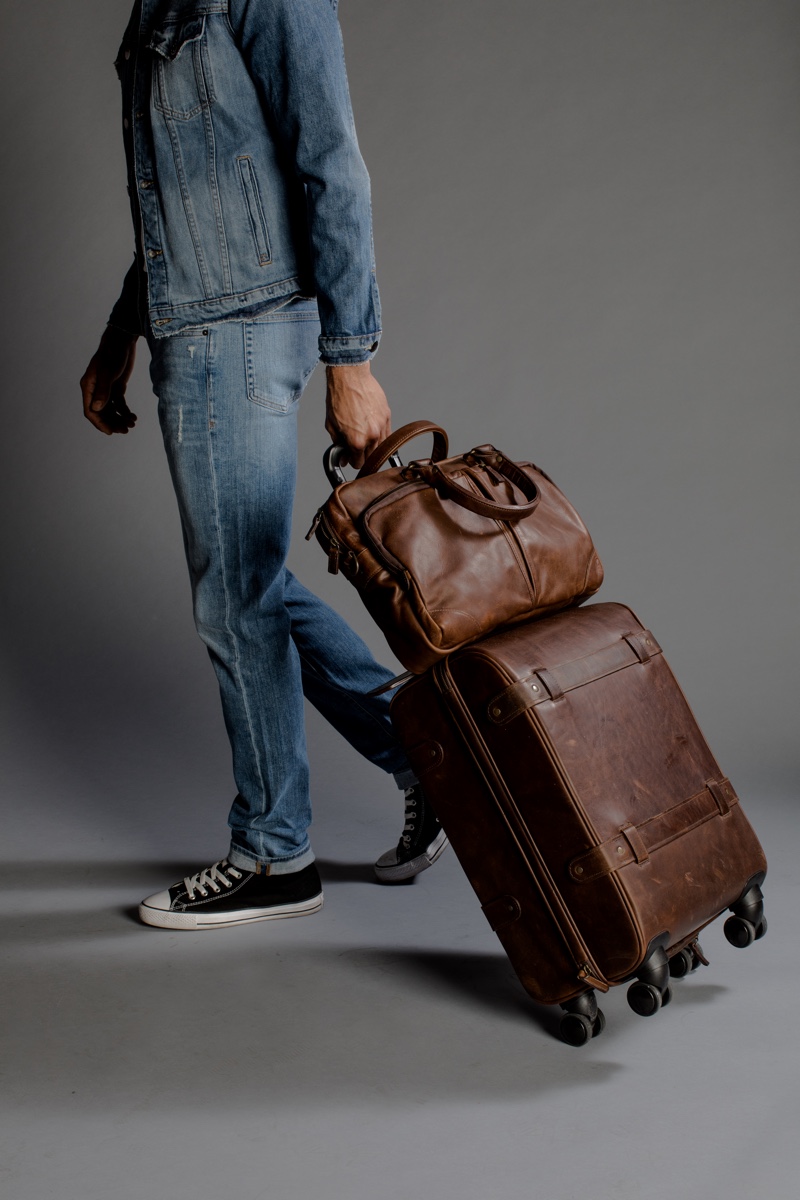 Zion wears shoes Converse, denim jacket and jeans Frame Denim. Travel bag set by Moore & Giles in saddle brown leather.