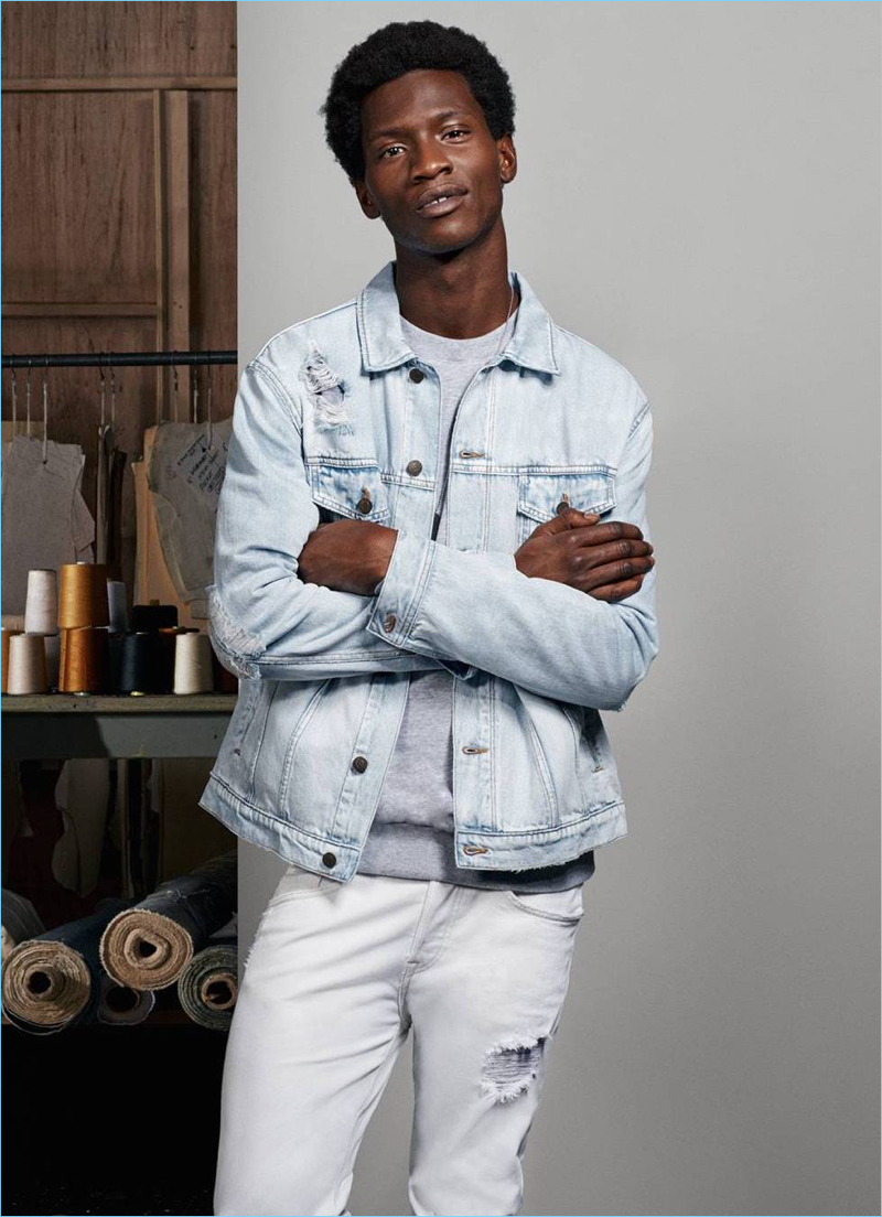 Connecting with H&M, Adonis Bosso wears a denim jacket, sweatshirt, and white skinny jeans.
