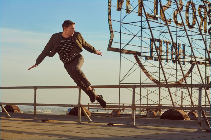 Nathan Mitchell wears a bomber jacket, striped sweater, trousers, and sneakers for H&M.