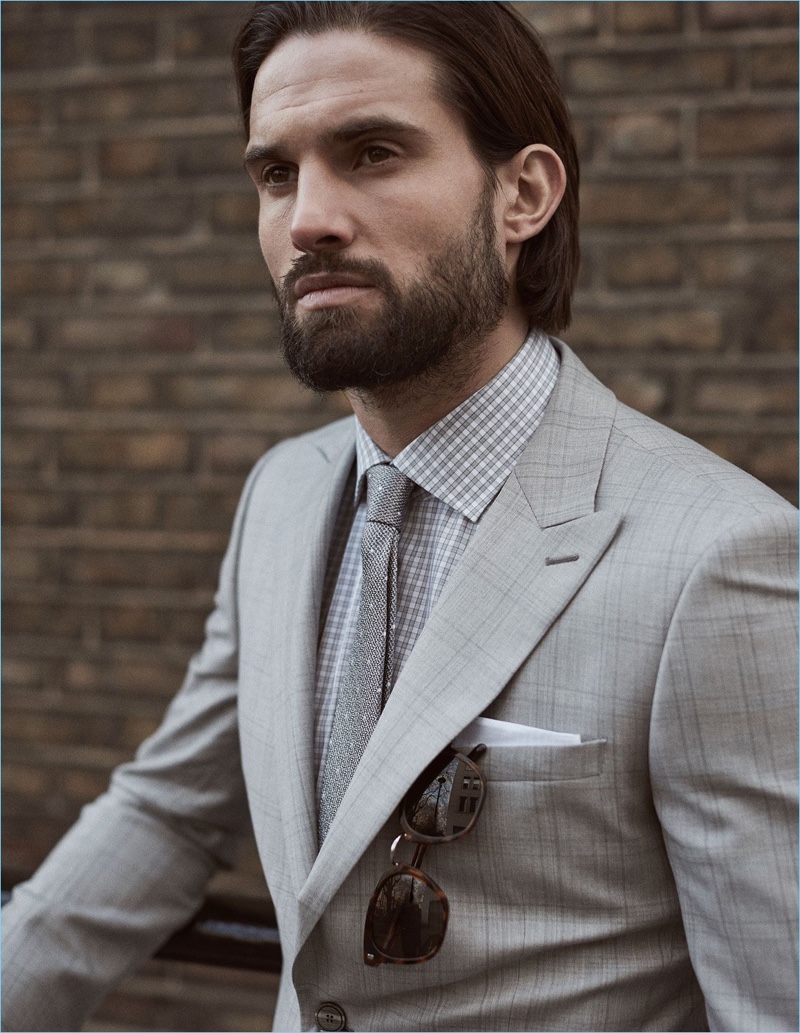 Donning shades of grey, Jamie Jewitt wears a Reiss suit, check shirt, tie, and sunglasses.