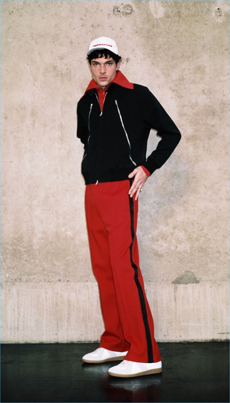 Sporting red, black, and white, Luka Isaac wears an Off-White baseball cap and Maison Margiela jacket. He also rocks a Balenciaga pullover, Maison Margiela track pants and sneakers.