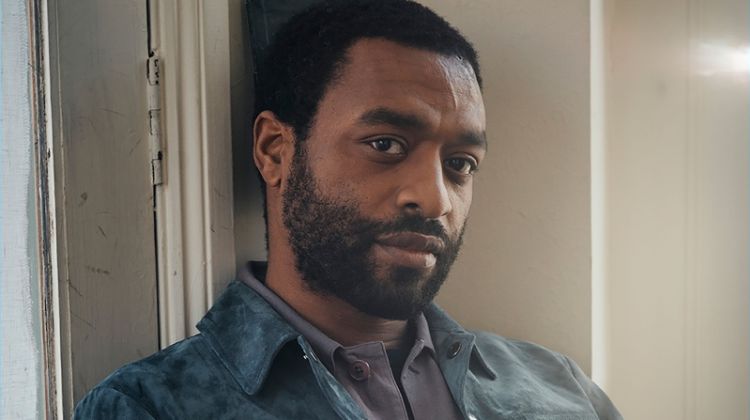 Sitting for a photo, Chiwetel Ejiofor dons a Tom Ford t-shirt and suede jacket. The actor also wears a Dries Van Noten shirt and Berluti trousers.