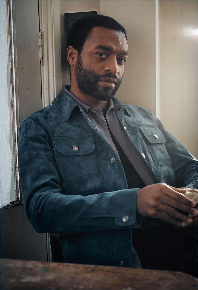 Sitting for a photo, Chiwetel Ejiofor dons a Tom Ford t-shirt and suede jacket. The actor also wears a Dries Van Noten shirt and Berluti trousers.