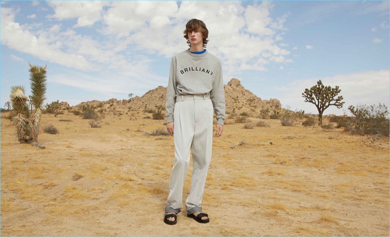 Taking to the desert, Benno Bulang wears a box logo sweatshirt and print t-shirt by A Brilliant Brand. Going monochromatic, he also sports Tarkek Classic cotton trousers by GmbH with Maison Margiela multi-strap leather sandals.