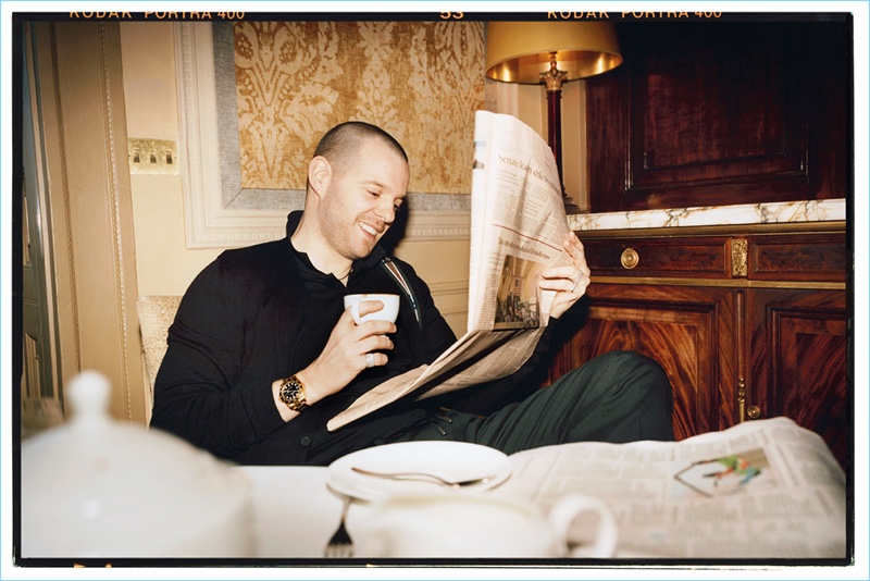 Reading the newspaper, Mike Skinner rocks a Fendi cardigan, Saint Laurent shirt, and Gucci drawstring trousers.