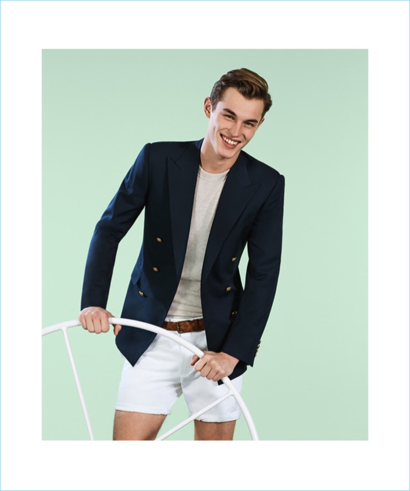 All smiles, Kit Butler is ready for travel to the French Riviera. He wears a POLO Ralph Lauren double-breasted blazer with a sweater and shorts.