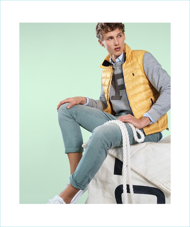 Nautical style from POLO Ralph Lauren is front and center. Here, Bram Valbracht wears a yellow down vest with a sweatshirt. He also sports a POLO oxford shirt, sneakers, and jeans.