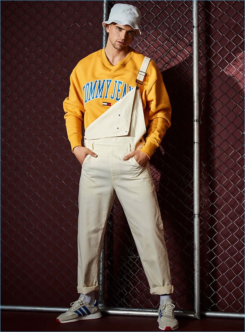 River Viiperi rocks LE 31 overalls with a Tommy Jeans sweatshirt in yellow. He also wears an Adidas Originals bucket hat.