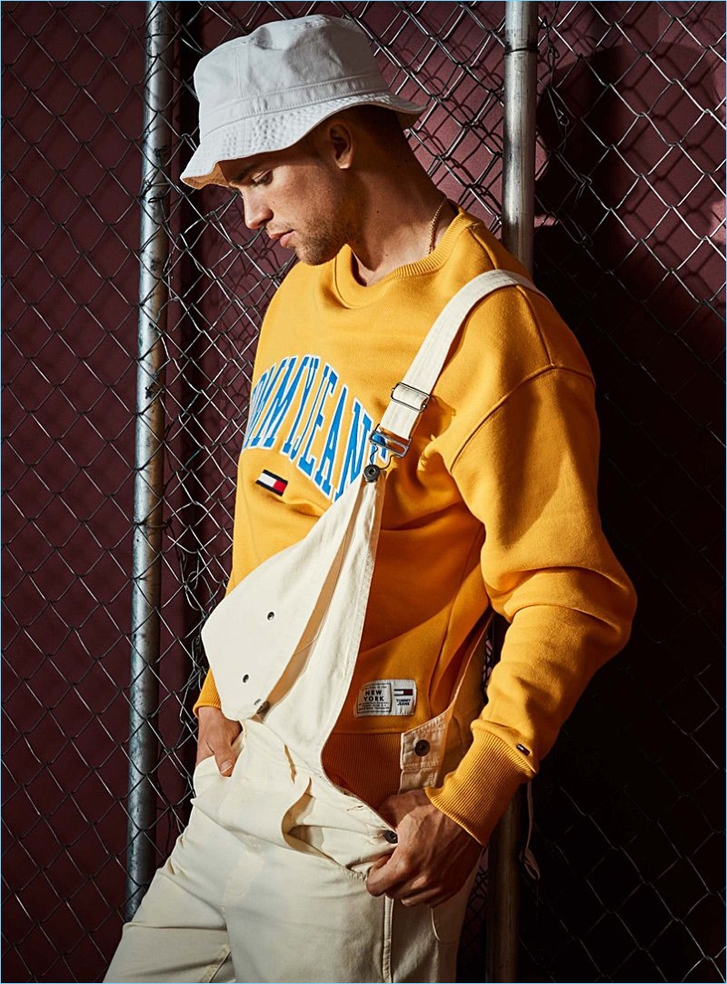 Embracing 90s style, River Viiperi wears LE 31 overalls with a yellow Tommy Jeans sweatshirt. The model also rocks an Adidas Originals bucket hat.