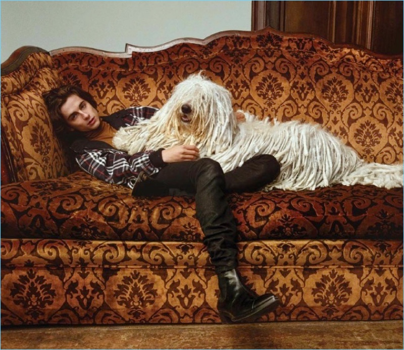 Posing with a dog, Timothée Chalamet wears a Gosha Rubchinskiy x Burberry jacket. He also dons a Bally turtleneck, Saint Laurent jeans, and Berluti boots.