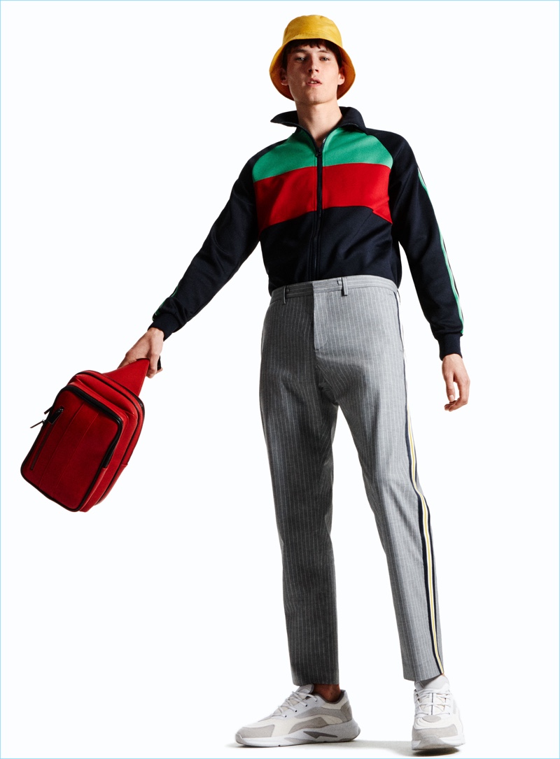 Embracing retro-inspired style, Frederik Ruegger wears a color-block jacket with pinstripe trousers by Zara Man. Frederik also rocks a bucket hat, sneakers, and crossover messenger bag from the Spanish brand.