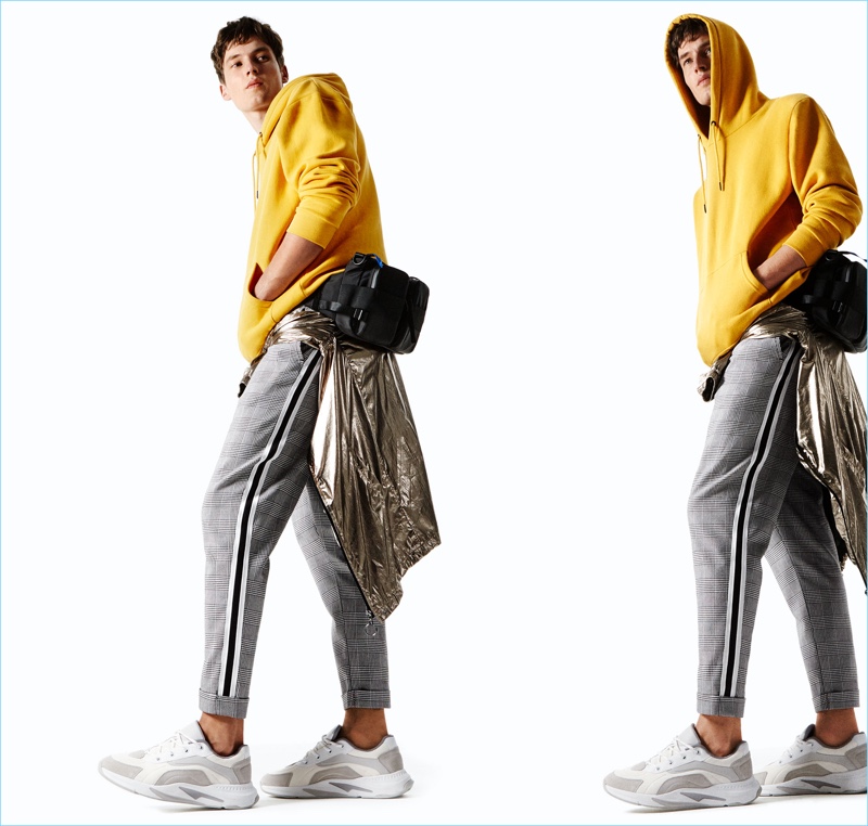 Model Frederik Ruegger wears a yellow sweatshirt, check trousers, a metallic jacket, belt bag, and leather sneakers from Zara Man.