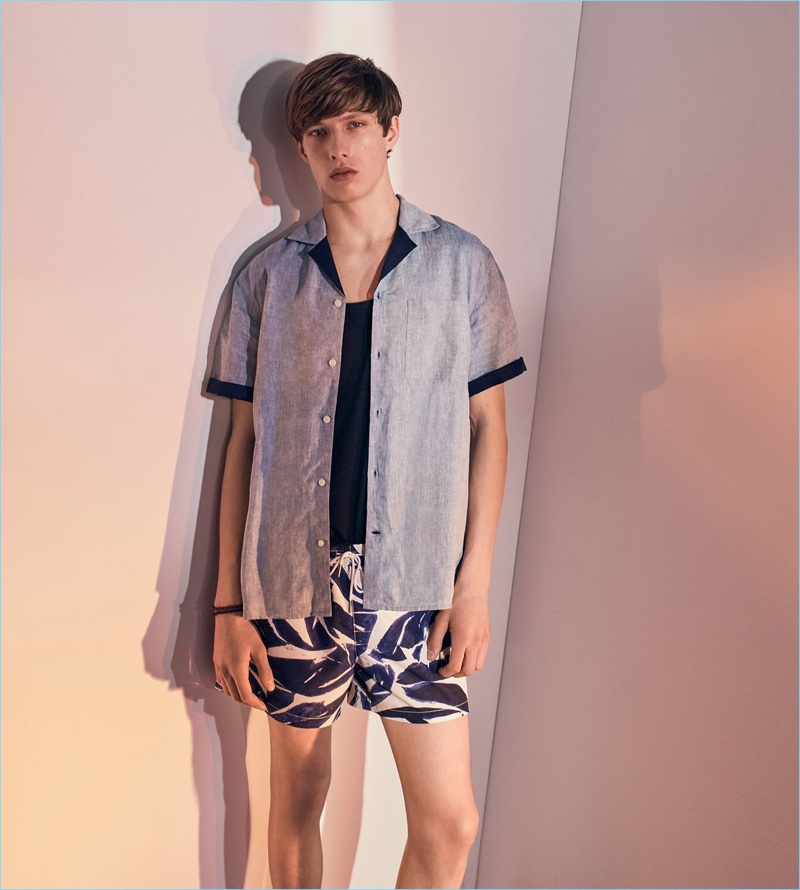 Ready to hit the beach, Gideon Yendell wears a Club Monaco tank, camp collar linen shirt, and leaf print swim trunks.