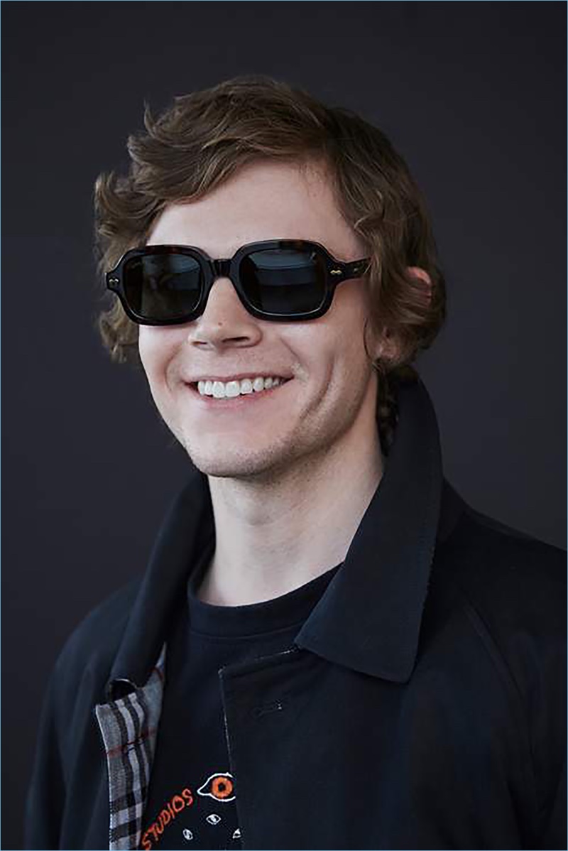 All smiles, Evan Peters wears a Burberry coat, Acne Studios sweatshirt, and Gucci sunglasses.