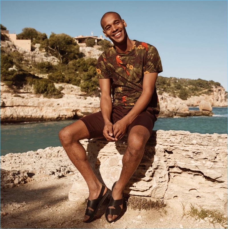 All smiles, Sacha M'Baye sports a tropical print t-shirt, burgundy chino shorts, and sandals by H&M.