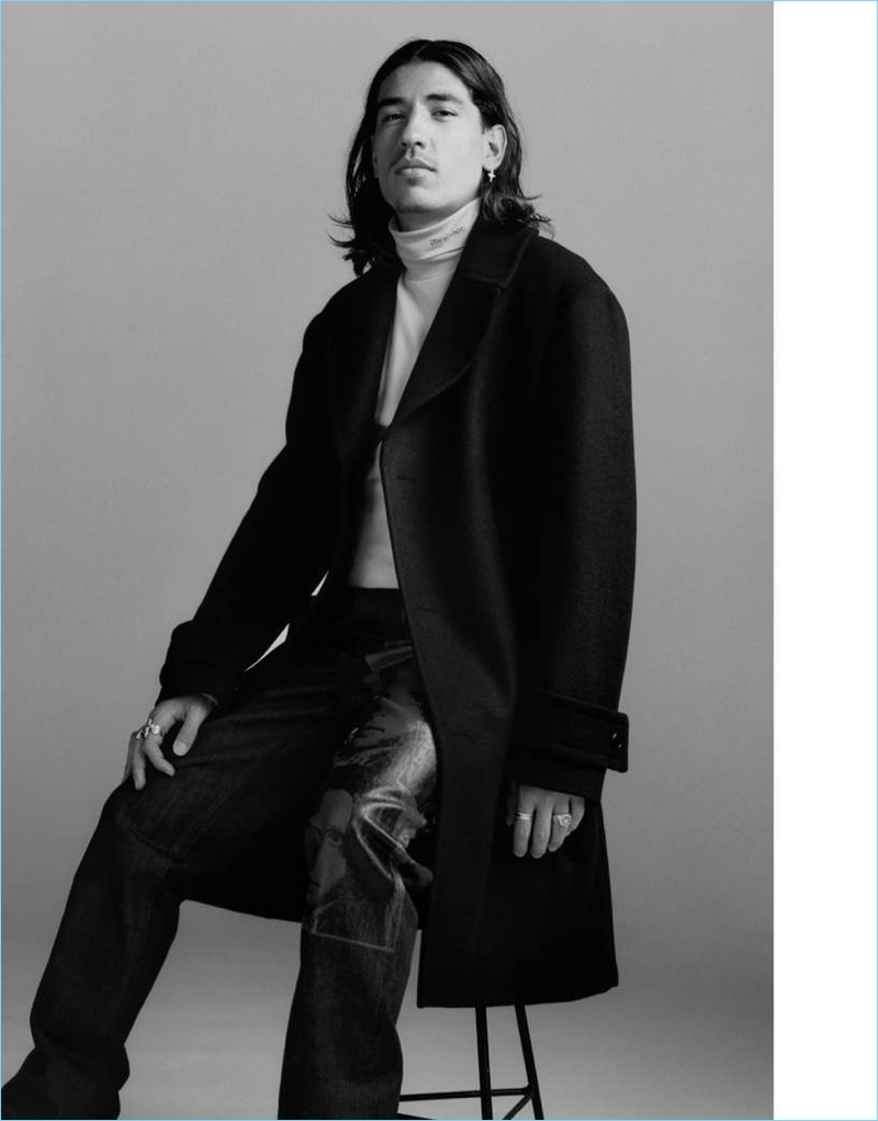 Clad in Calvin Klein, Héctor Bellerín wears a wool overcoat, denim jacket, turtleneck, and printed jeans.