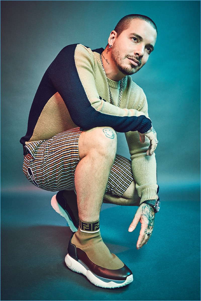 Singer J Balvin sports a Fendi Family pullover and FF logo sock sneakers. He also rocks MSGM plaid shorts, Ben Baller x Takashi Murakami necklaces, Ben Baller rings and a Tag Heuer watch. 