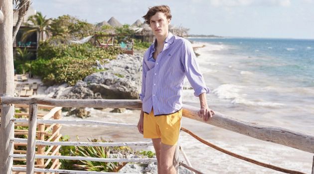 Into the Blue: Tim Dibble Models Vacation Style for Matches Fashion Embracing summer style, Tim Dibble wears a Lanvin striped shirt, Marané swim shorts, and a logo charm necklace by Saint Laurent.