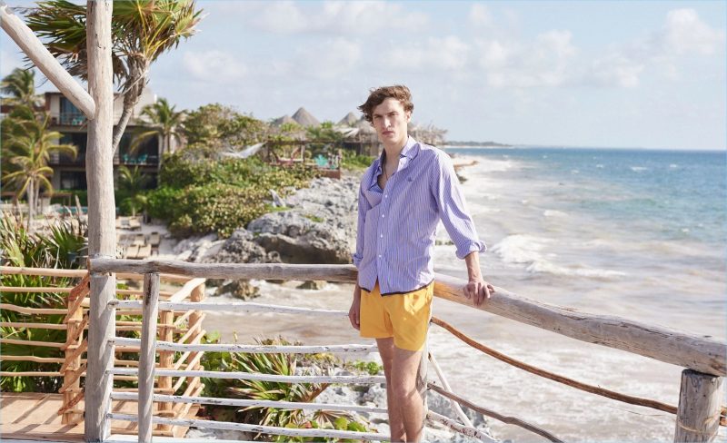 Embracing summer style, Tim Dibble wears a Lanvin striped shirt, Marané swim shorts, and a logo charm necklace by Saint Laurent. 