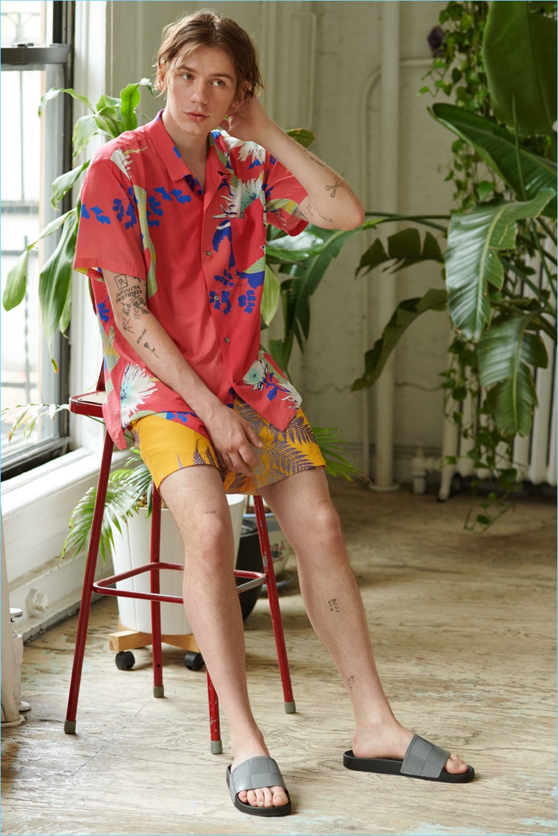 Embracing a summer look, Luca Bertea models a Double Rainbouu Hawaiian shirt and swim trunks with Adidas by Raf Simons sandals.