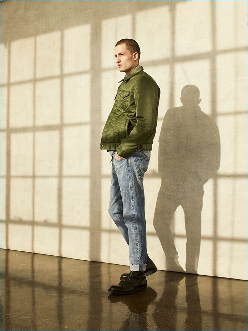 Delivering a side profile, Frederik Woloszynski sports an army green jacket with light wash denim jeans by Levi's.
